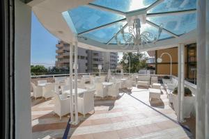 uma varanda com cadeiras e mesas brancas e um tecto de vidro em Hotel Soleblu em Rimini