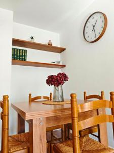 a dining room table with a vase of flowers and a clock at Apartamento Pena Furada in Ribadeo