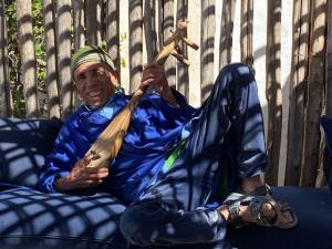 an older man sitting on a couch holding a stick at Hotel-Restaurant Le Kaouki in Sidi Kaouki