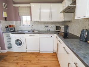 Una cocina con gabinetes blancos y lavadora. en Sandy Shore, en Chathill