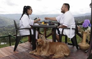a man and a woman sitting at a table with a dog at Amore Mio Glamping in Jenesano +2 photos