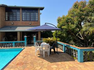 a table with chairs and an umbrella next to a pool at Chácara das Pedras Acolhedor, Alegria, Refúgio in Piracaia