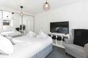 a white bedroom with a bed and a tv and a chair at The Hamlet - North East Escapes in Tynemouth