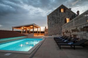 a swimming pool with chairs next to a building at Didova kuća, kamena vila sa bazenom u blizini Rogoznice in Podorljak