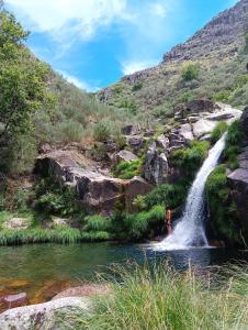 a person standing in a stream in front of a waterfall at Tienda de Campaña en Ecoaldea Vegana Espiral en Plena naturaleza con comida y cena incluida in Passos
