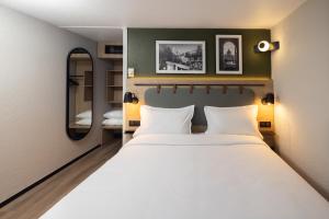 a bedroom with a large white bed and a mirror at Campanile NATURE - Alençon in Alençon