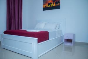 a white bedroom with a white bed with a red blanket at Spacious & Serene 3-Bedroom Condo at Kai Villa in Accra