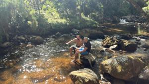 two people sitting on rocks in a stream at Vibe Coffee Container CATUAÍ VERMELHO in Pedra Menina