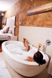 Una donna sdraiata in una vasca da bagno con un bicchiere di vino di African Rock Hotel and Spa a Kempton Park