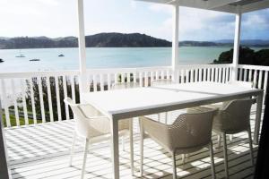 a white table and chairs on a porch with the ocean at Daisy Harbour View - Waterfront! in Raglan