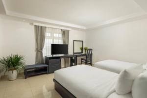 a bedroom with two beds and a desk with a television at Kay Han Riverfront Hotel Da Nang in Danang