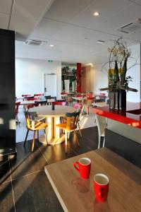 un comedor con mesas, sillas y tazas rojas en una mesa en Colmar Hotel en Colmar