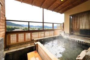 a hot tub in a house with a large window at Ryokan Biyunoyado in Yamanouchi