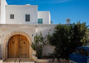 a building with a wooden door and a blue car at Dar Nejma - Djerba Houch in Erriadh