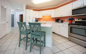 eine Küche mit weißen Schränken und zwei grünen Stühlen an einer Theke in der Unterkunft Phoenix on the Bay 1121 condo in Orange Beach