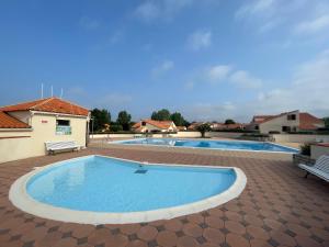 a large swimming pool in a patio with a bench next to it at Charmante Maison proche mer avec piscine collective in Brem-Sur-Mer