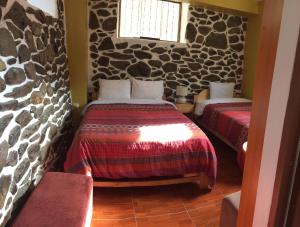 two beds in a room with stone walls at Kamma Guest House in Ollantaytambo