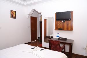 a bedroom with a bed and a desk with a tv on the wall at Villa Serenity Le Sejour Pondicherry in Kottakupam