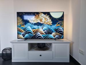 un televisor en un stand con una pintura en él en Wellnesshaus Dorfblick mit Outdoor-Jacuzzi und Infrarotkabine, NEU!, en Dreis-Brück