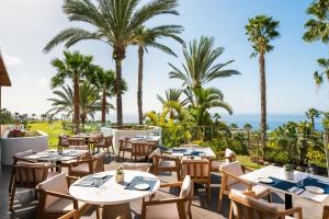 a restaurant with tables and chairs and palm trees at Los Jardines de Abama Suites in Guía de Isora