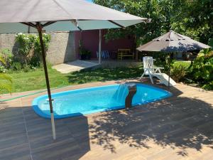 a swimming pool with an umbrella and a chair and a table at Quarto com Ar-condicionado há 600 metros da Praia de Setiba in Guarapari