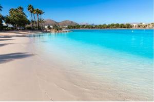 a beach with palm trees and blue water at Apartamento Arcoiris, con piscina y junto a playa de Alcudia in Alcudia