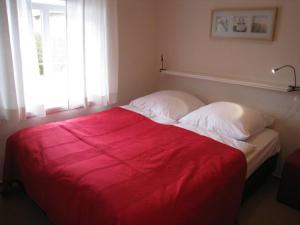 a bed with a red blanket on it in a bedroom at Sommergarten in Wyk auf Föhr +13 photos