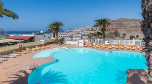 a swimming pool with chairs and palm trees in a resort at Calle Goya 108 in Arguineguín