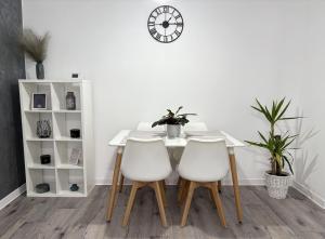 a table with three white chairs and a clock on the wall at Inga Apartment in Turda