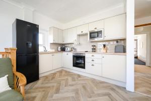 a kitchen with white cabinets and a black refrigerator at Oxendon Oasis- Luxury Hot Tub Retreat in Market Harborough