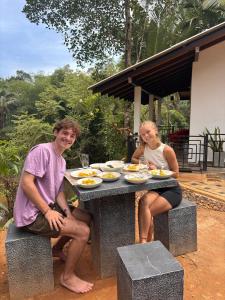 Un uomo e una donna seduti a un tavolo con del cibo di Rainforest River Bay a Deniyaya