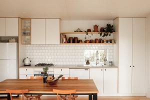 a kitchen with white cabinets and a wooden table at Eco Shipping Container Home in Kilcunda