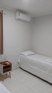 a white bedroom with a bed and a night stand at Hotel Pinheiros in Nossa Senhora da Glória