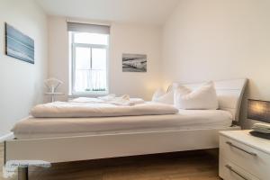een witte slaapkamer met een groot bed met een raam bij Ferienwohnung 1 im 'BÖTTCHER HUUS' in Langeoog