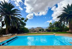 a swimming pool with palm trees and a blue sky at Villa Casa Lilo, en jardin grande,con una gran piscina, con pérgola y barbacoa in Arona