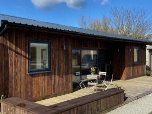 a wooden cabin with a deck with a table and chairs at Wheal Rock - Luxury 2 Bed Lodge in St. Agnes