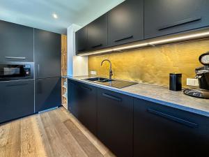 eine Küche mit schwarzen Schränken und einer Spüle in der Unterkunft Alpine Apartment Goldquell - Infrarot Kabine, National Park Sommerkarte und Bergblick in Rauris