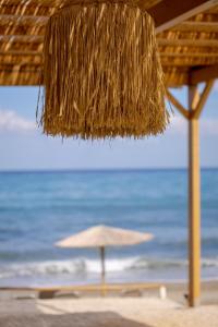 a straw umbrella on a beach with the ocean at Odysseus Aparthotel in Plataniás