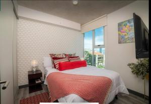 ein Schlafzimmer mit einem Bett mit roten Kissen und einem Fenster in der Unterkunft Dreamliner at 11s, City Views and Wonderland Vibes! in Hatillo