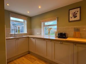 a kitchen with white cabinets and a sink and a window at Cosy Carnegie Cottage close to Dornoch Golf Course in Dornoch