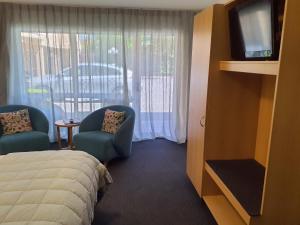 a hotel room with a bed and two chairs and a television at Tuscana Motor Lodge in Christchurch