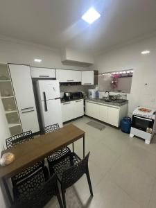 une cuisine avec des armoires blanches et une table et des chaises en bois dans l'établissement Casa de Praia com piscina, à Santa Cruz Cabrália