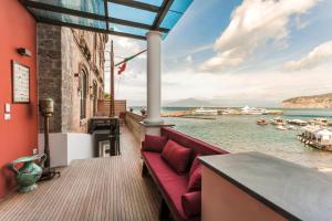 un divano rosso su un balcone con vista sull'acqua di Yacht Club Capo Cervo Suites B&B a Sorrento