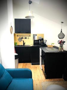 a kitchen with black cabinets and a blue couch at L'Arôme - Studio intimiste à deux pas du tram et des facultés in Talence