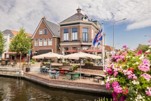 a building with tables and umbrellas next to a river at Boutique Hotel Joure - centrum & haven in Joure