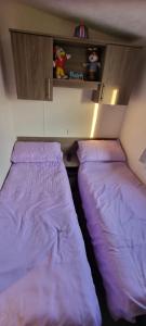 two beds in a small room with purple sheets at The Cwtch Caravan Trecco Bay in Newton