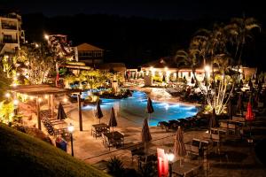 a pool with umbrellas and chairs and a resort at night at Tauá Hotel & Convention Caeté in Roças Novas