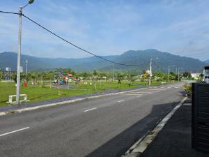 an empty road with a playground and mountains in the background at Ipoh Meru Landed Homestay TropiCasa 28 in Ipoh