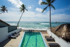 a swimming pool next to the ocean with palm trees at Lucky Seven Hikkaduwa in Hikkaduwa