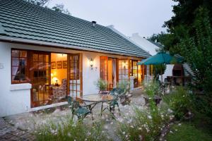 ein Haus mit einem Tisch, Stühlen und einem Sonnenschirm in der Unterkunft Swallows Nest Country Cottages in Stormsrivier